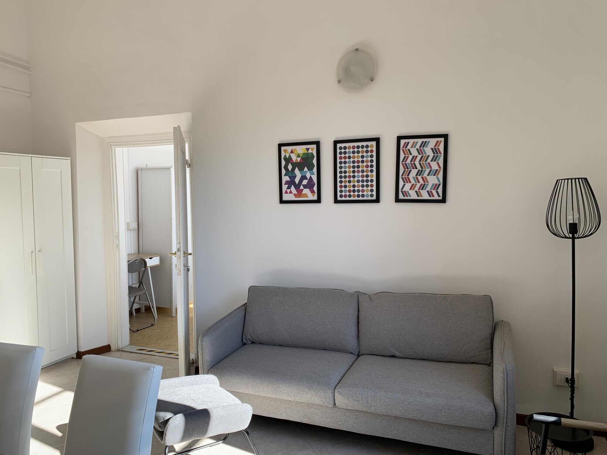 A modern living room with a grey sofa, a small table, and a floor lamp. There are three framed artworks on the wall.