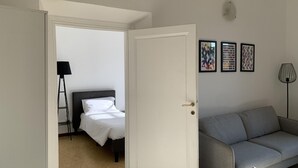 A room with a bed, a grey sofa, and a door leading to another room.