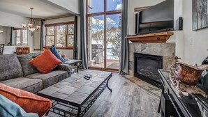 A spacious living room with a fireplace, a large TV mounted above it, and a cozy seating area with a sofa and a coffee table. - The Oak Lane Chateau: with Private Hot Tub, Close to Golf, Free Ski Shuttle!! (Breckenridge)
