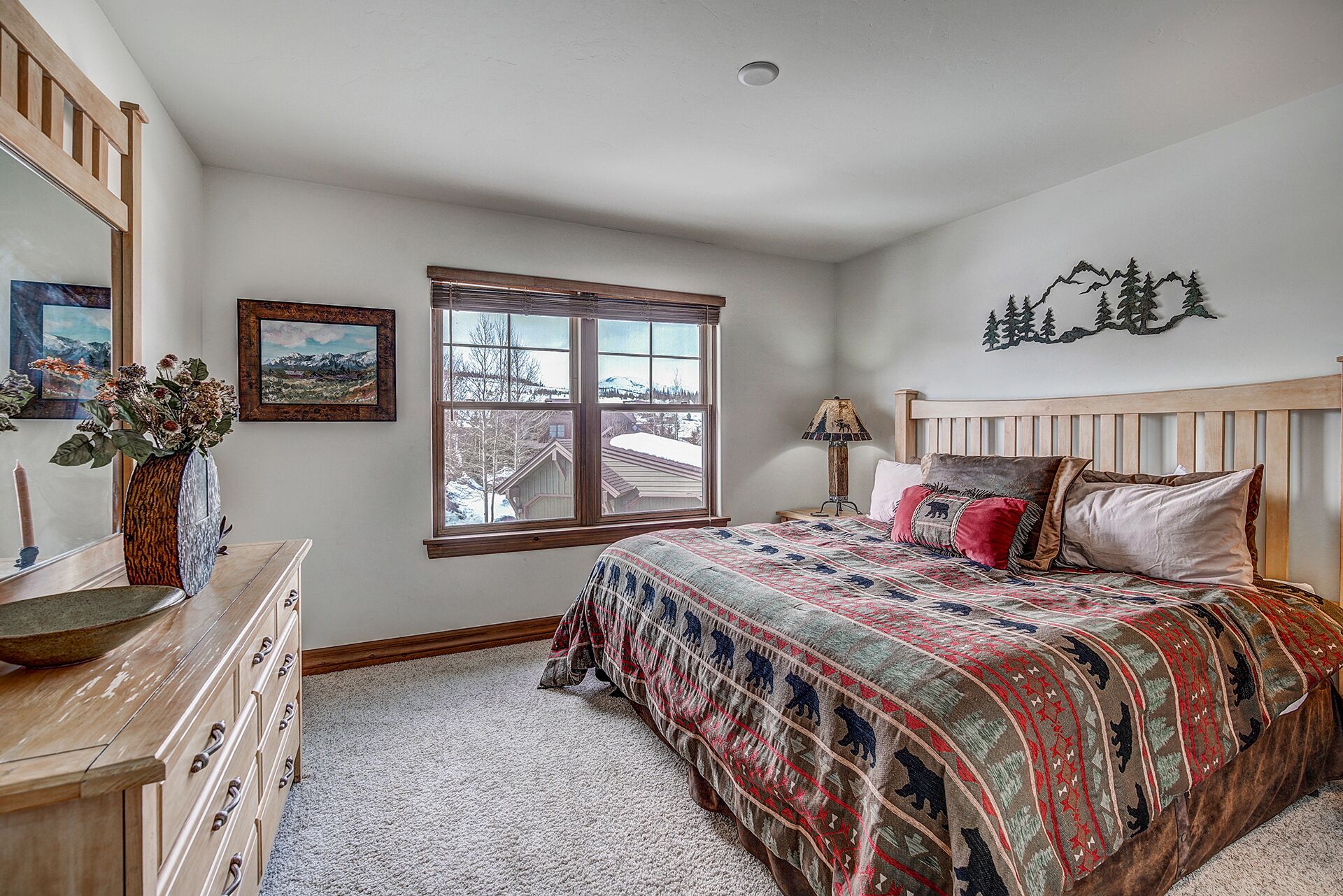 A bedroom with a large bed, a dresser, a window with a view of a snowy landscape, and a wall-mounted decoration.