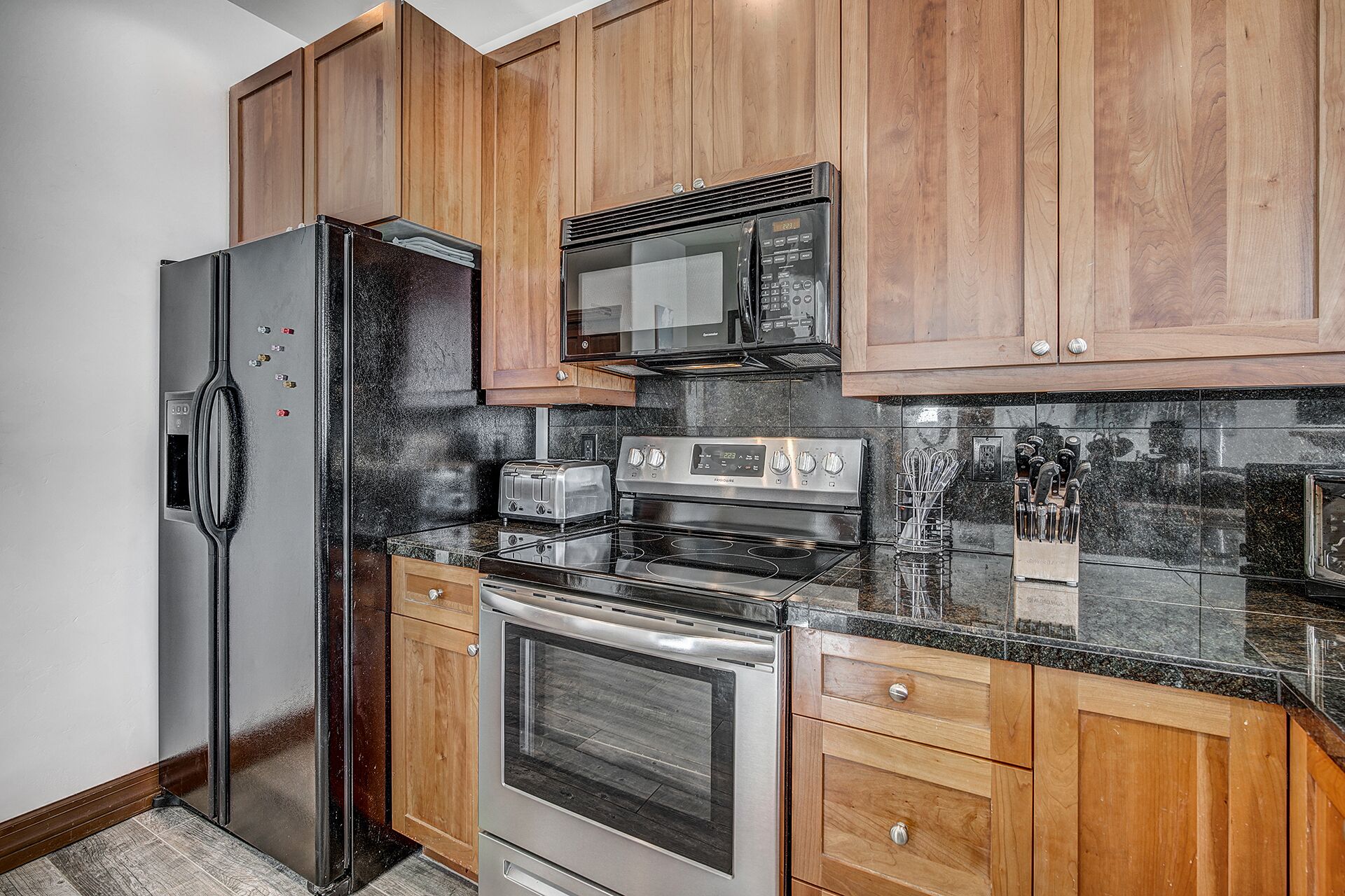 A kitchen with wooden cabinets, a stainless steel refrigerator, a microwave, a stove, and a toaster.