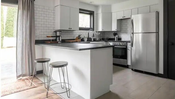 Eine moderne Küche mit weißen Schränken, einer zentralen Kochinsel mit Hockern, einem Kühlschrank und einem Backofen.