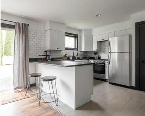 Una cocina moderna con armarios blancos, una isla central con taburetes, un refrigerador y un horno.