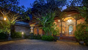 A courtyard with a paved walkway, surrounded by lush greenery and traditional architecture. - Kudesa Homestay (Sukawati)