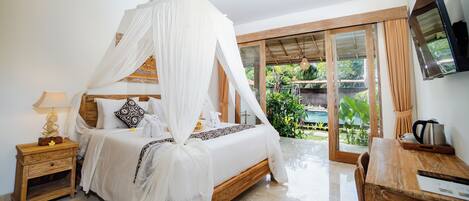 A bedroom with a canopy bed, a wooden nightstand, a desk, and a TV mounted on the wall.