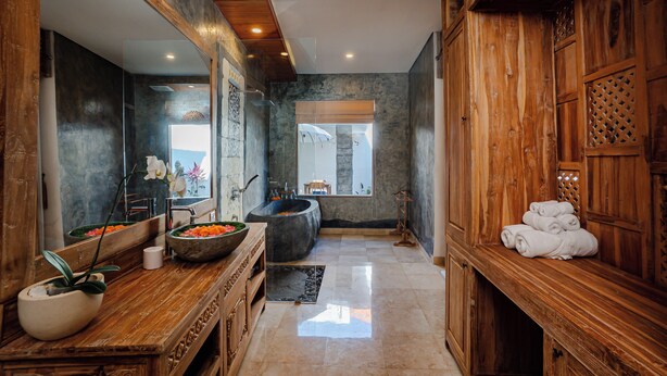 A modern bathroom with a wooden vanity, a large mirror, a stone sink, and a bathtub. - Kudesa Homestay (Sukawati)
