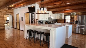 A spacious kitchen with a large island, wooden ceiling beams, and modern appliances. - Grand Spruce Lodge, Lakefront near Talkeetna & Denali State Park (Trapper Creek)