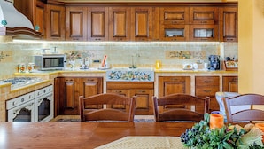 Una cocina con armarios de madera, microondas, estufa y comedor con sillas.