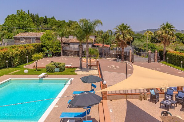 Ein Poolbereich mit Liegestühlen und Sonnenschirmen, umgeben von einem angelegten Garten und Blick auf eine Wohngegend.