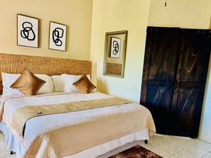 Una cama con cabecera, almohadas y una manta. En la pared hay cuadros enmarcados.
