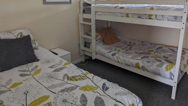 Een slaapkamer met stapelbed met wit frame, een nachtkastje en een bed met een bedspreider met bladmotief.