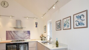 A modern kitchen with built-in appliances, a dining area with a table set for two, and artwork on the walls. - Blue Neptune (Lyme Regis)