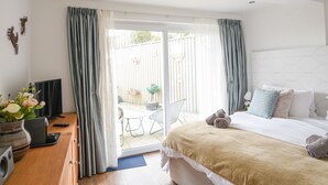 A bedroom with a bed, a desk with a computer, a window with curtains, and a view of the outside. - Blue Neptune (Lyme Regis)