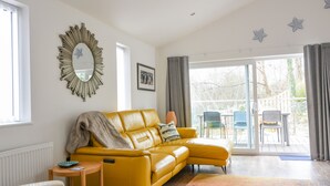 A modern living room with a yellow sofa, a round mirror, and a large window with a view of the outdoors. - Blue Neptune (Lyme Regis)