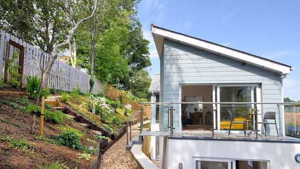 A modern two-story house with a balcony, a covered outdoor seating area, and a garden with a wooden fence. - Blue Neptune (Lyme Regis)