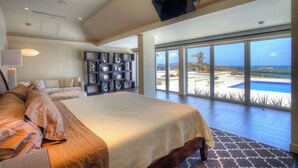 Un dormitorio amplio con una cama grande, una estantería empotrada y vista al océano a través de puertas correderas grandes.