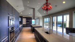 Una cocina moderna con armarios oscuros, electrodomésticos de acero inoxidable, una isla central y vistas al océano a través de grandes ventanales.