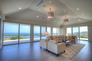 A spacious living room with a large sofa set, a coffee table, and a view of a coastal landscape through floor-to-ceiling windows. - Beautiful 7.7 acre estate with a huge home and stunning views of the Caribbean (Christiansted)