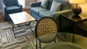 A modern living room with a blue sofa, a glass coffee table, a patterned armchair, and a floor lamp. - The Residences Olympia (Makati)