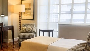 A hotel room with a bed, a chair, a small table, a lamp, and a window with a view. - The Residences Olympia (Makati)