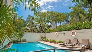 A swimming pool with lounge chairs and lifebuoys on a sunny day. - The Residences Olympia (Makati)