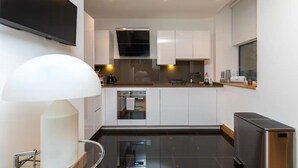 Una cucina moderna con mobili bianchi, forno integrato e televisore a schermo piatto montato a parete.