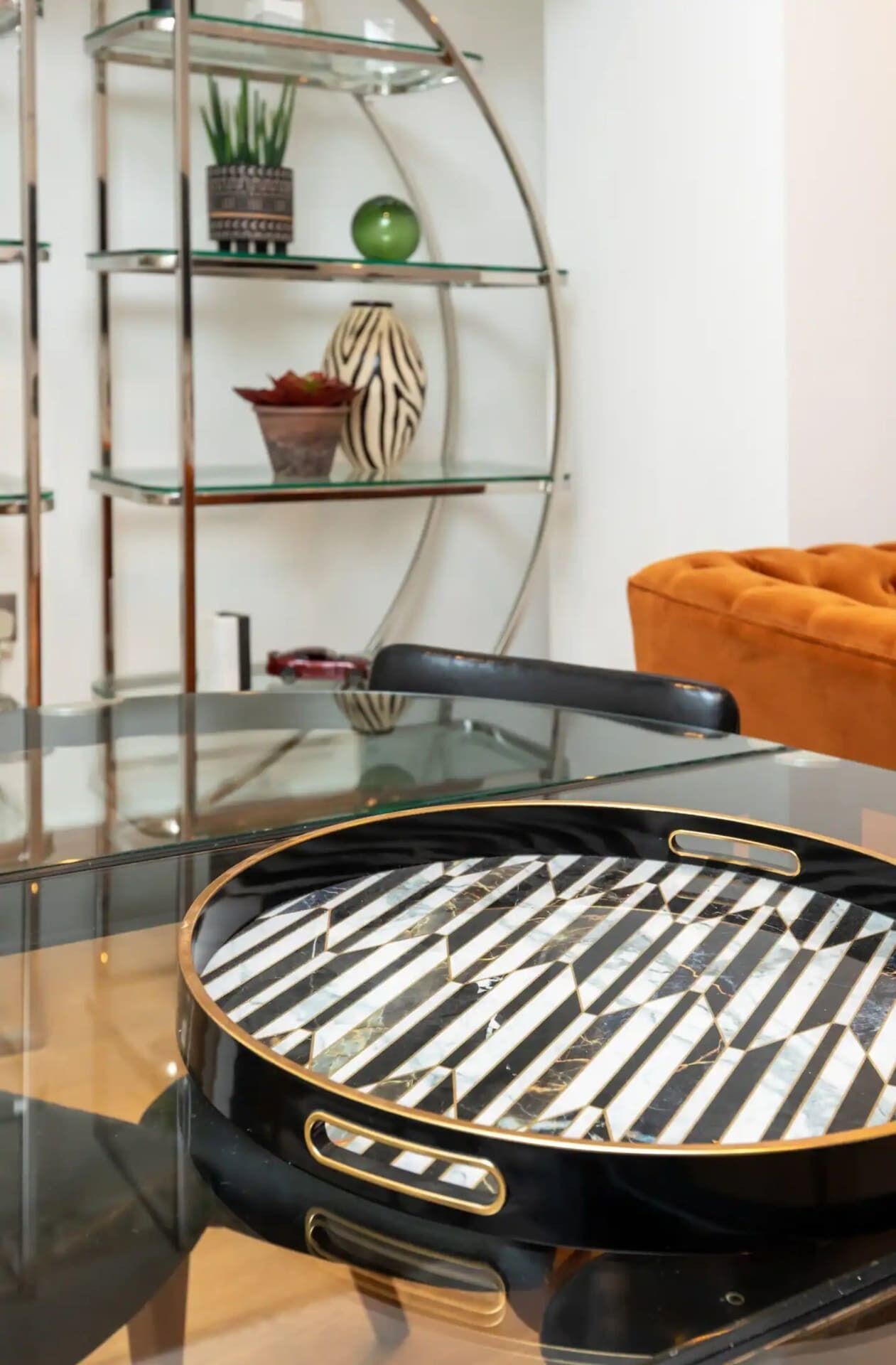 Une table à manger recouverte d’une nappe à motifs noir et blanc, avec un plateau en verre et une chaise dotée d’un coussin noir.