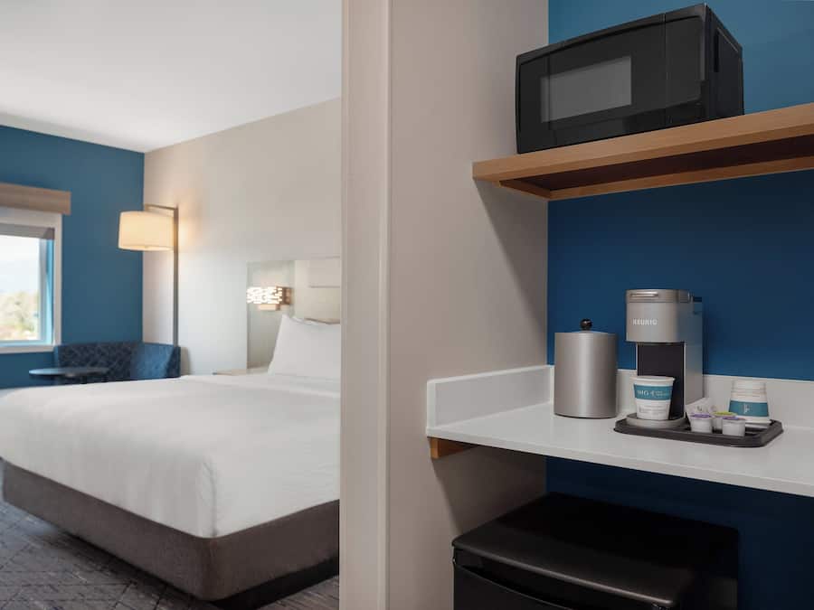 A hotel room with a bed, a desk, a microwave, a coffee maker, and a trash bin.
