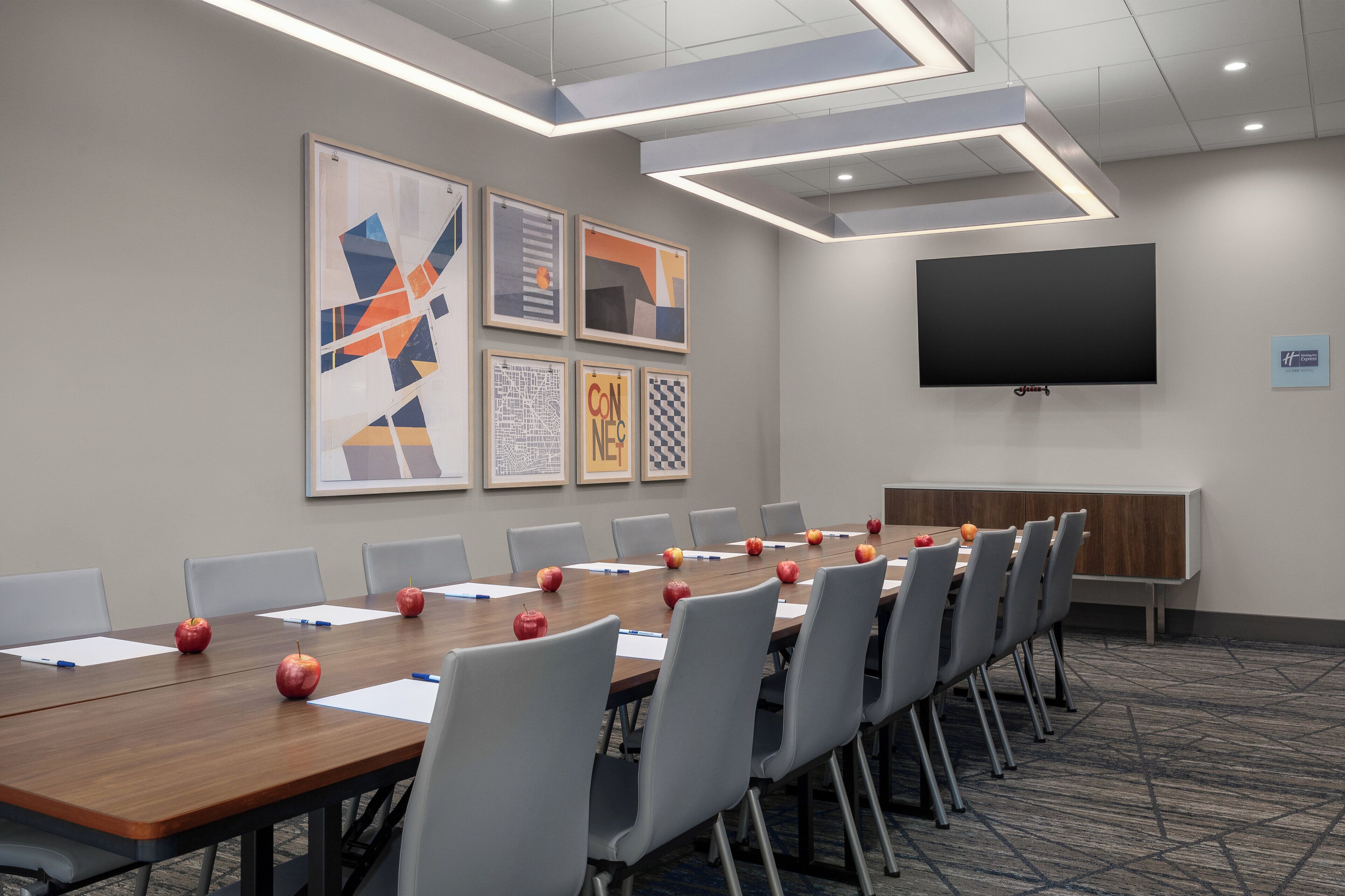 A conference room with a long table, chairs, apples, and framed artwork on the wall.