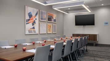 A conference room with a long table, chairs, apples, and framed artwork on the wall.