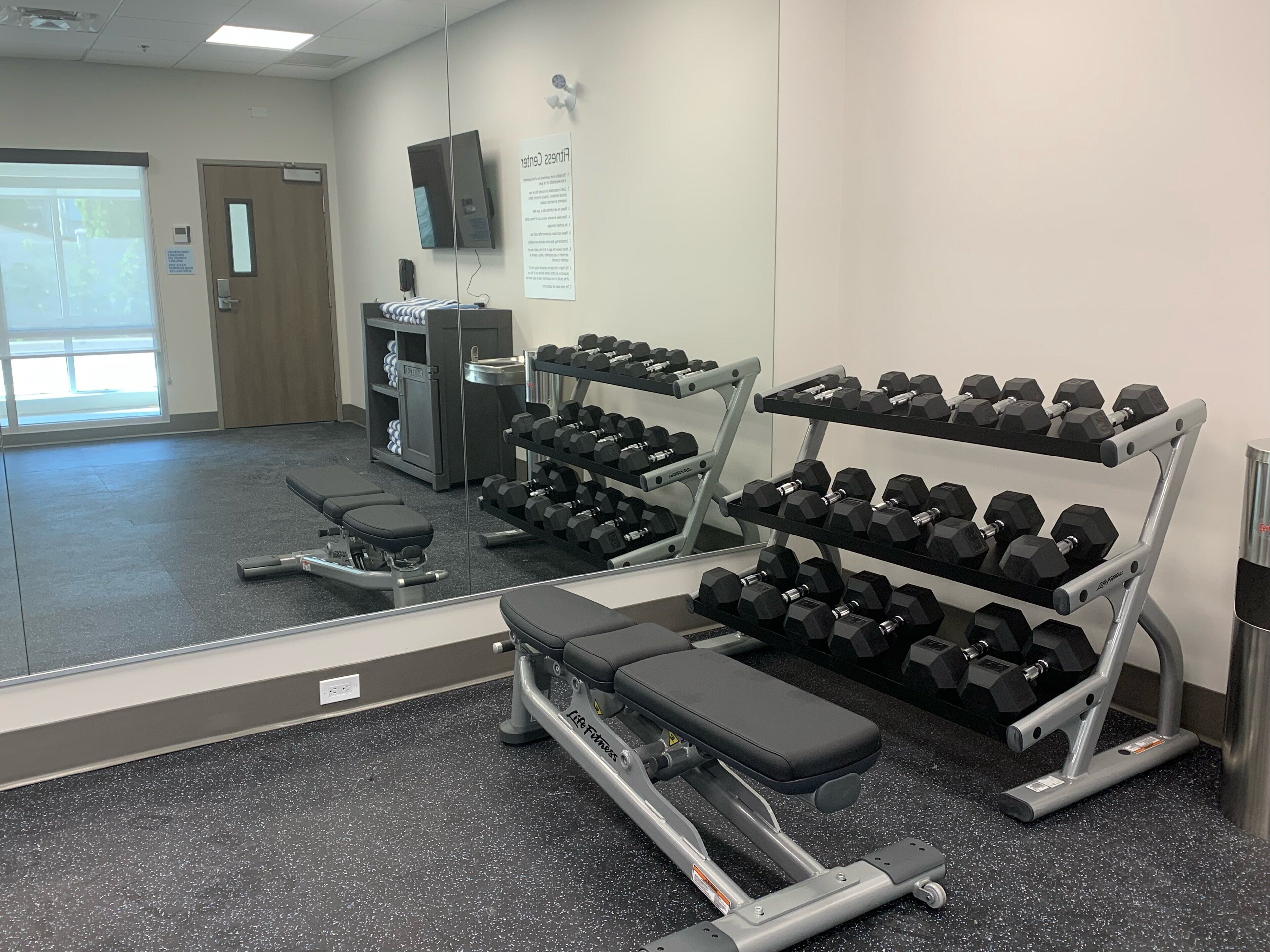 Un gimnasio con equipamiento de ejercicio, incluyendo mancuernas, bancos y una cinta de correr.