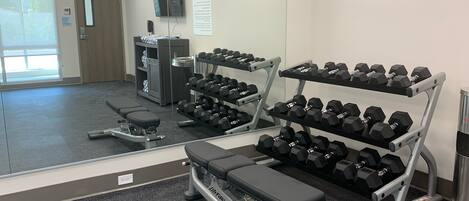 Un gimnasio con equipamiento de ejercicio, incluyendo mancuernas, bancos y una cinta de correr.