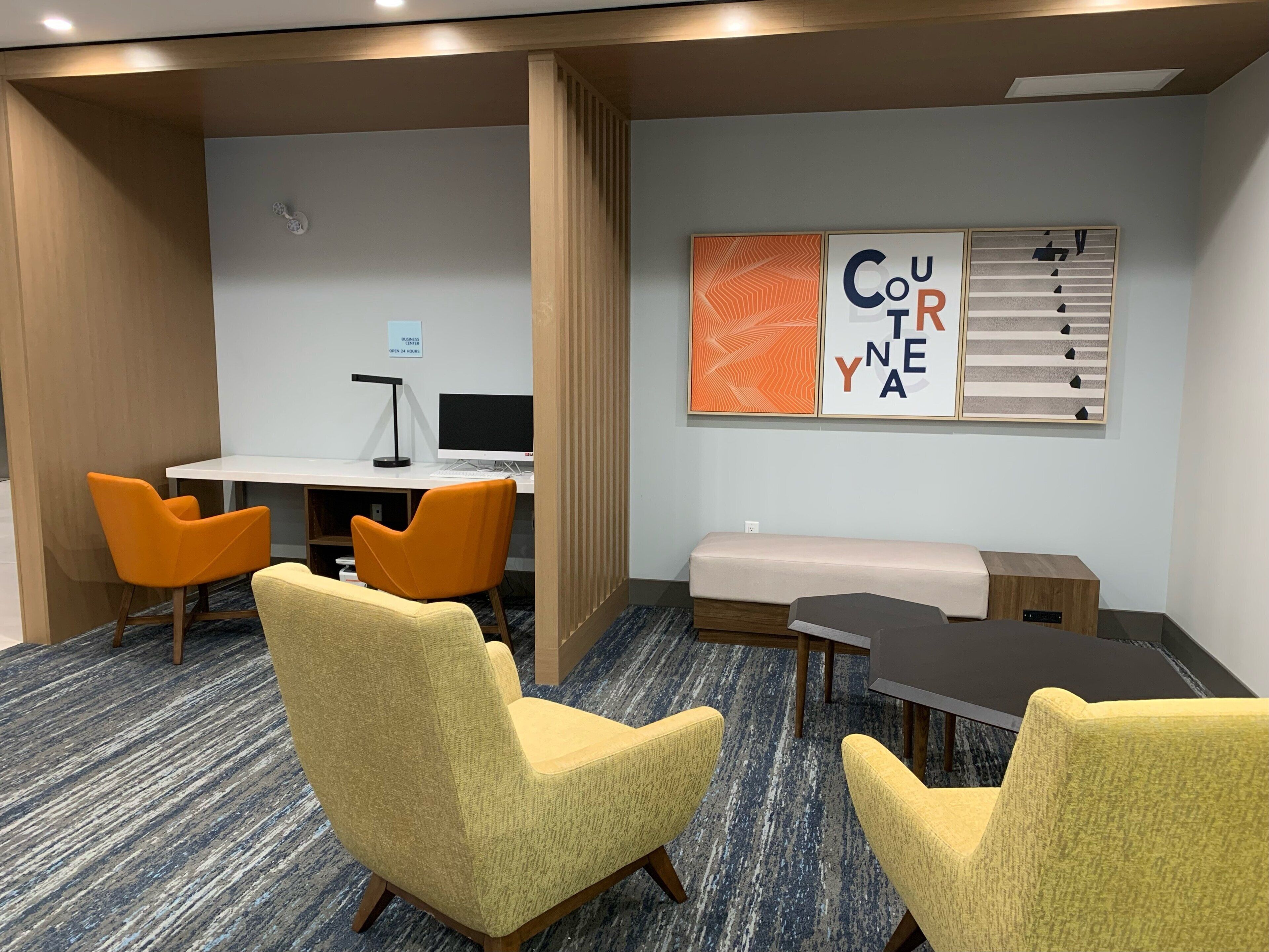 A conference room with a white desk, two orange chairs, a yellow sofa, and a large wall-mounted artwork.