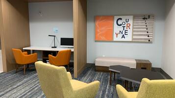 A conference room with a white desk, two orange chairs, a yellow sofa, and a large wall-mounted artwork.