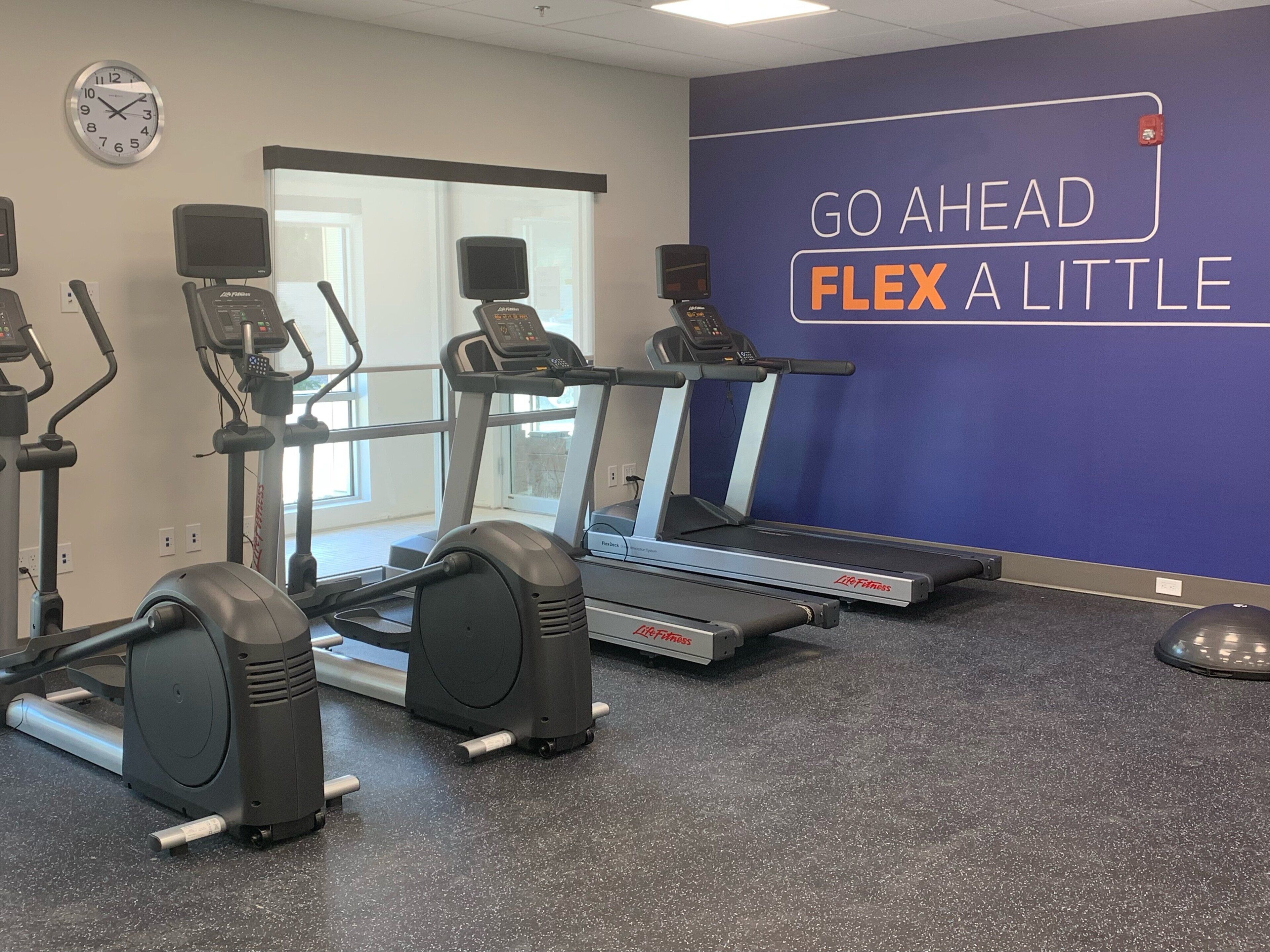 Ein Fitnessraum mit Laufbändern, Crosstrainern und einer Wand mit motivierenden Texten.