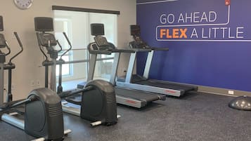 Ein Fitnessraum mit Laufbändern, Crosstrainern und einer Wand mit motivierenden Texten.