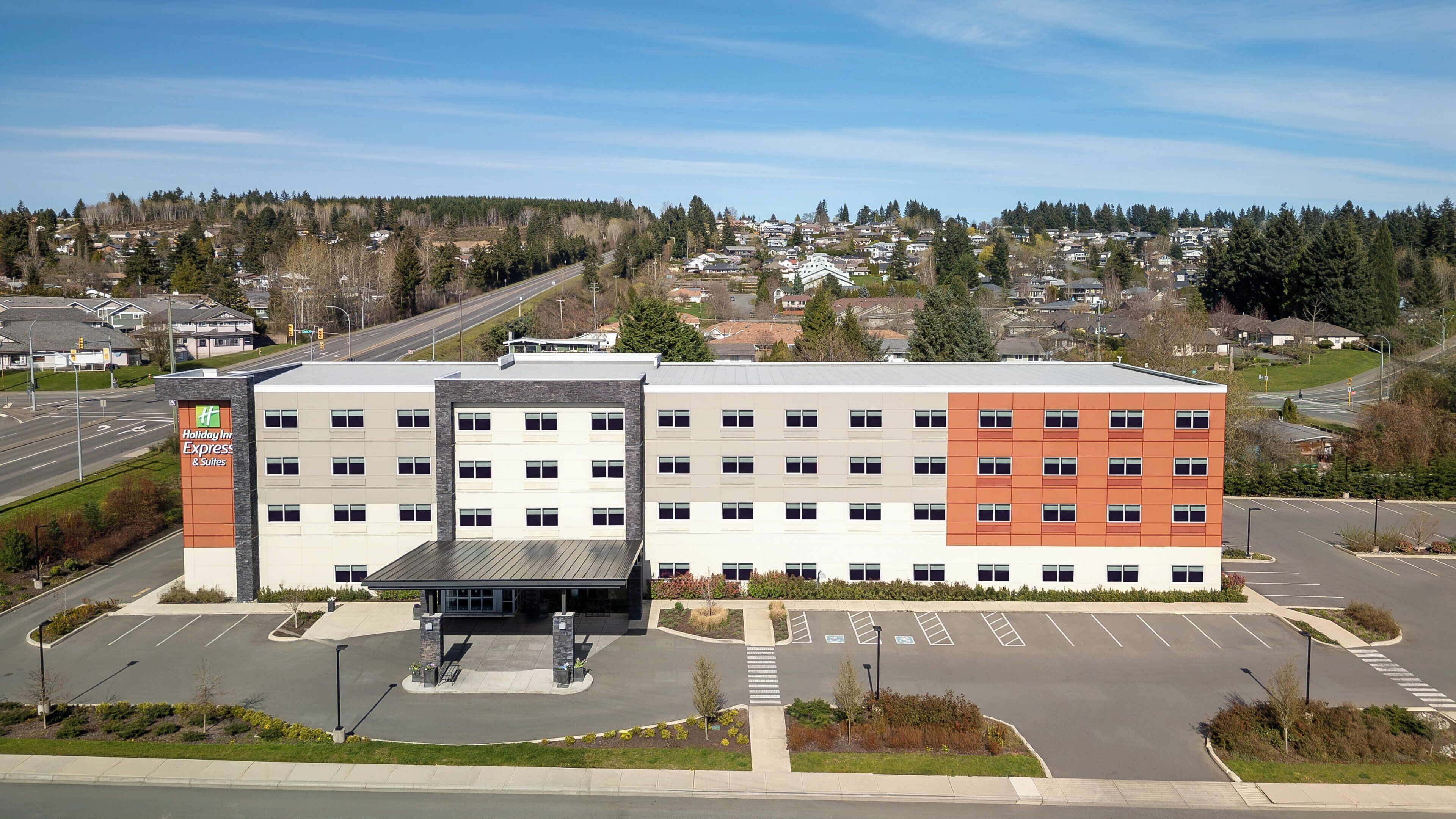 Un hôtel Holiday Inn Express & Suites doté d’un parking, avec une route visible au loin et une ville aux reliefs vallonnés en arrière-plan.