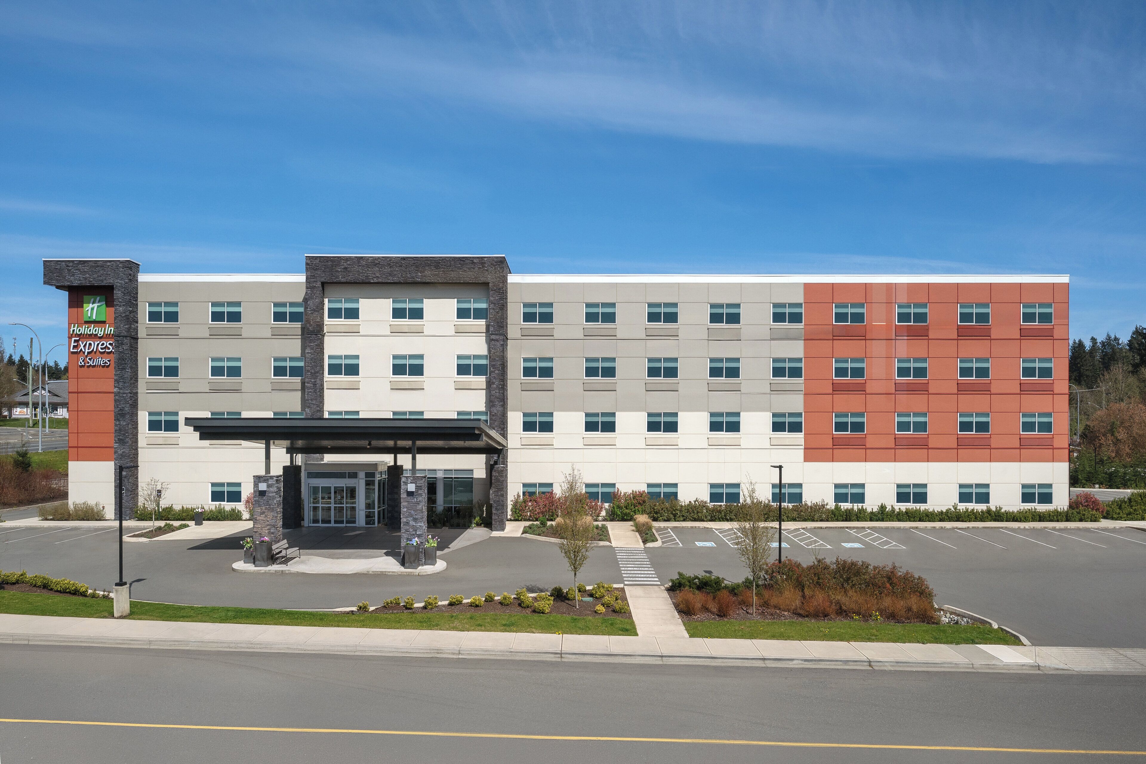 Un bâtiment Holiday Inn Express & Suites au design moderne, doté d’une entrée couverte et d’un parking.