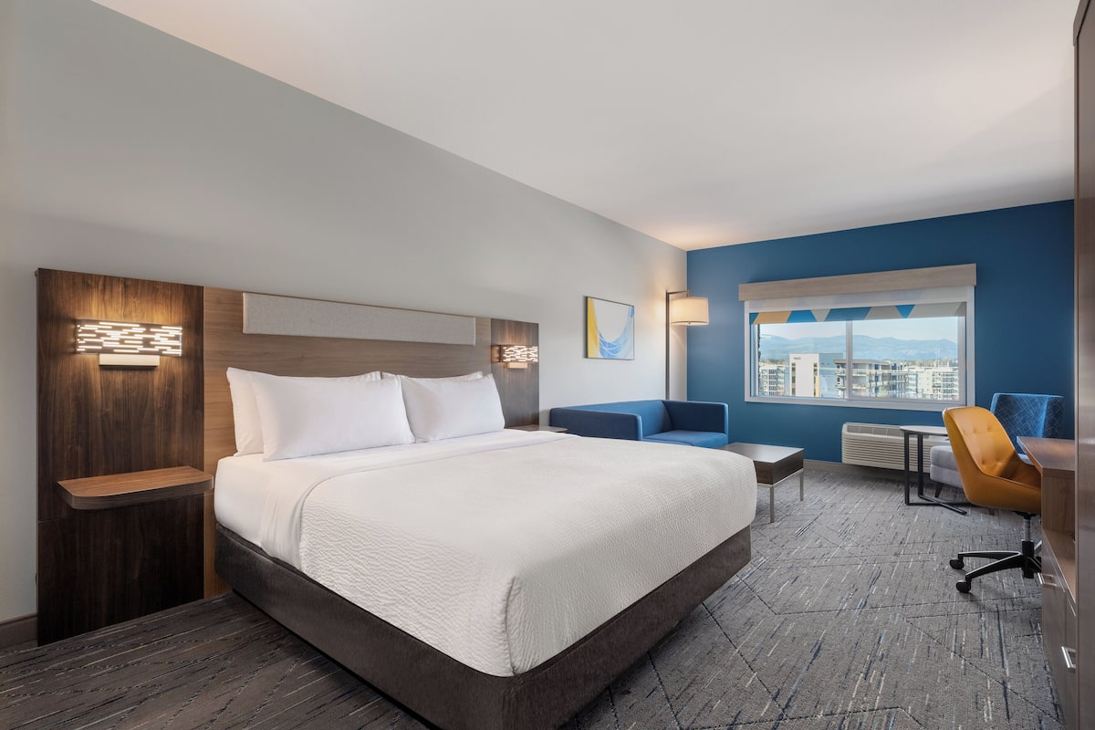 A hotel room with a large bed, a desk, a chair, and a view of the city.