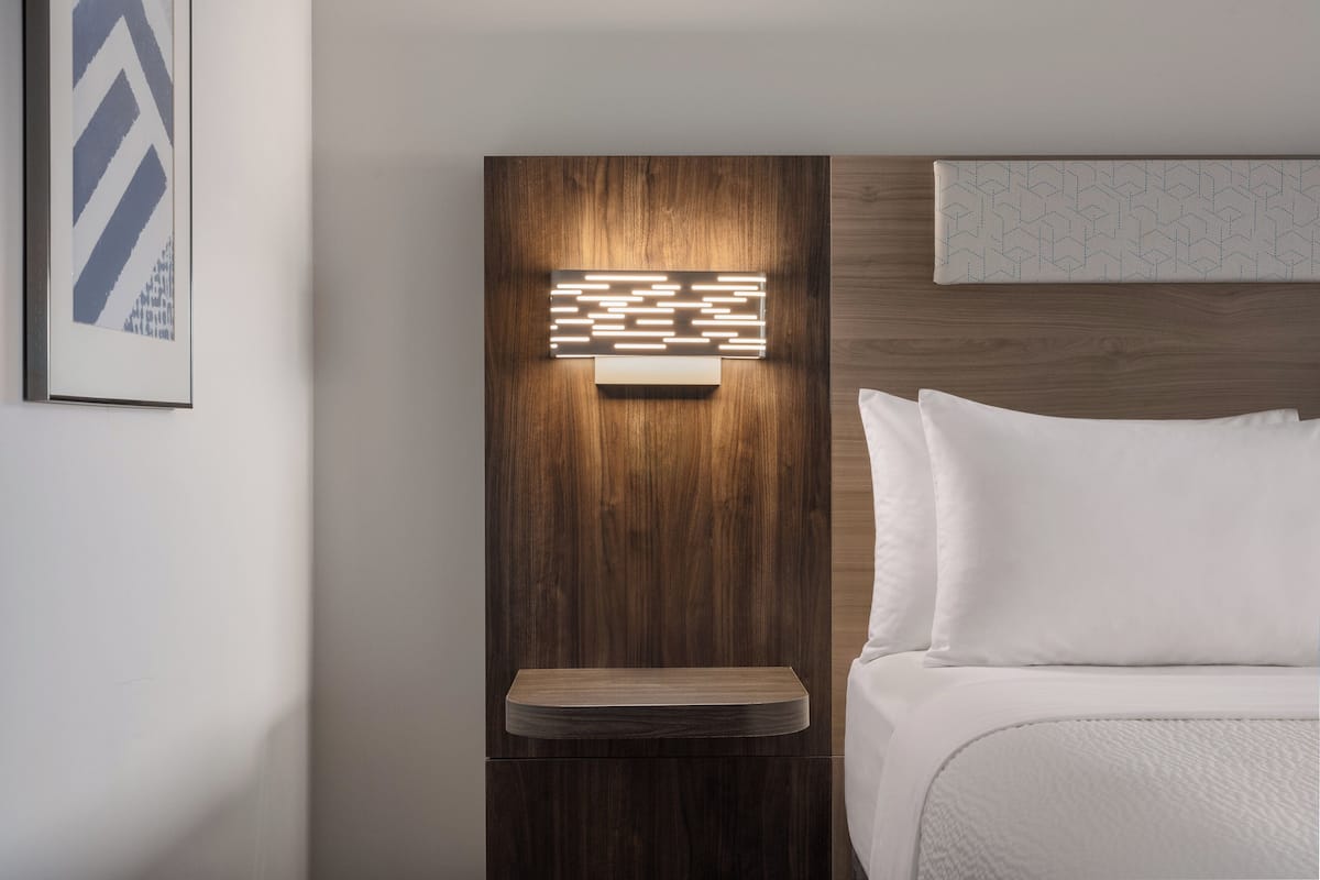 A hotel room with a wooden headboard, a bedside table, and a bed with white bedding.