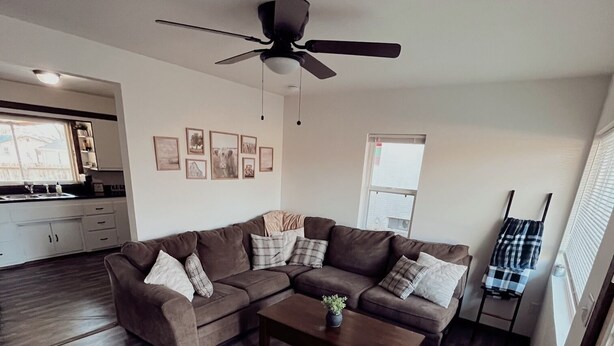 A spacious living room with a dark wood floor, a brown sectional sofa, a coffee table, and a ceiling fan. - Stockton Lakes’ Rustic Retreat - Cozy & Close (Stockton)