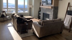Un salon doté d’une cheminée, d’un téléviseur fixé au-dessus et d’une grande fenêtre offrant une vue sur les montagnes.