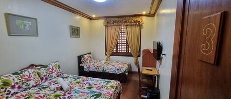 Quarto com duas camas, uma escrivaninha pequena, um espelho e uma janela com cortinas.