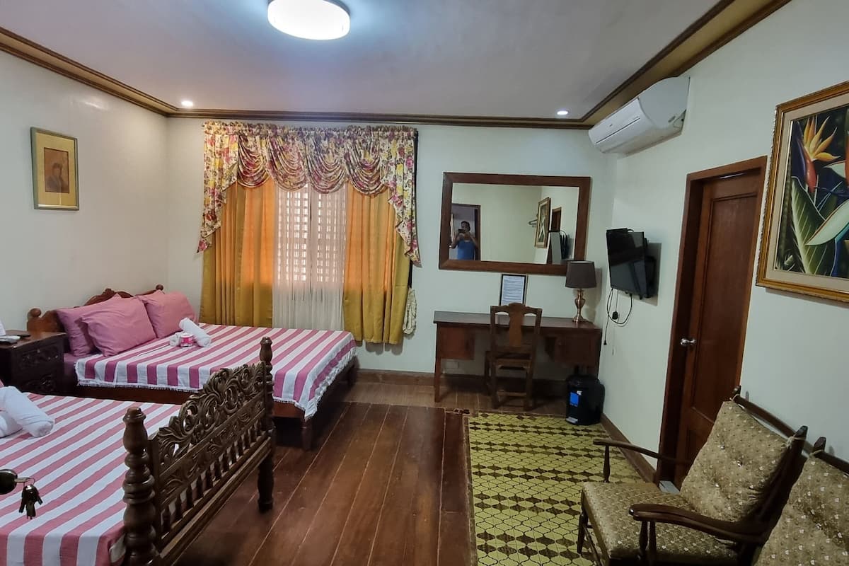 A room with two beds, a desk, a chair, and a large painting.