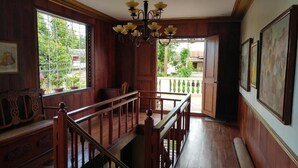 Interior de madera con una escalera, un candelabro y un balcón con vistas a zonas verdes.