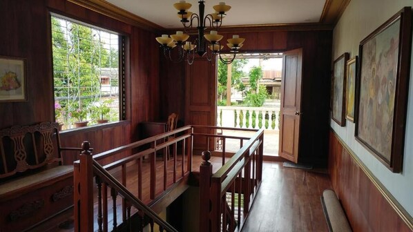 Interior de madera con una escalera, un candelabro y un balcón con vistas a zonas verdes.