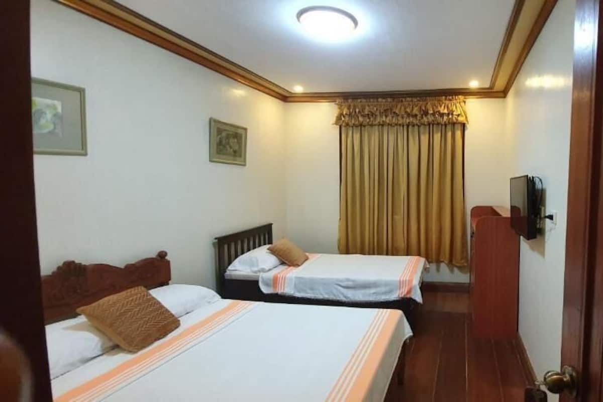 A hotel room with two beds, a wooden wardrobe, a television, and a door marked with the number 3.