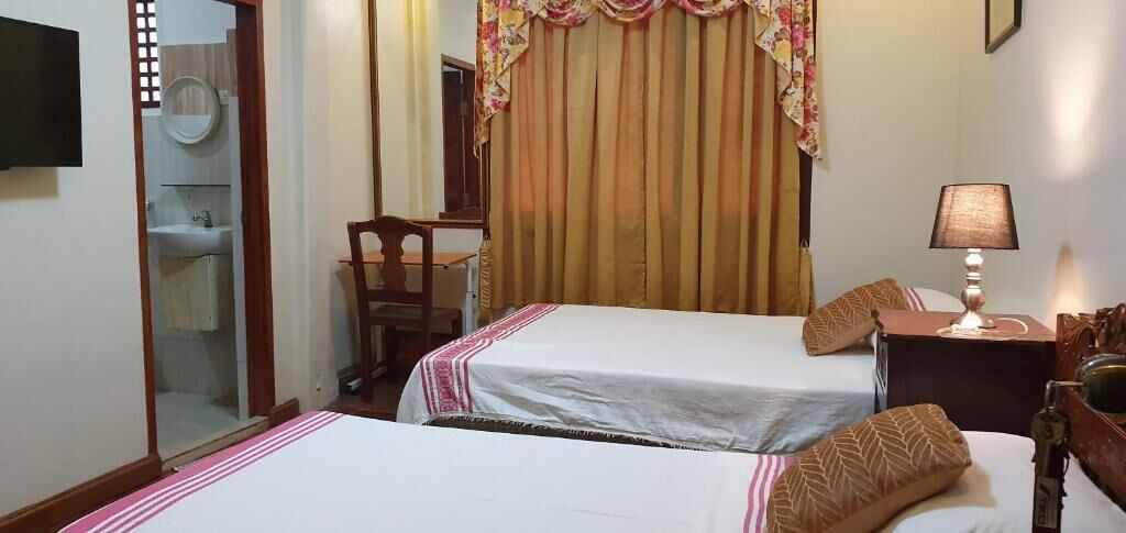 Una camera d'albergo con due letti, una scrivania, una sedia, una televisione e una lampada.