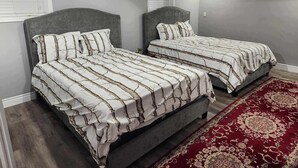 A bedroom with two beds, grey headboards, and a red patterned rug.