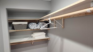 A storage closet with shelves holding folded blankets and a drying rack.